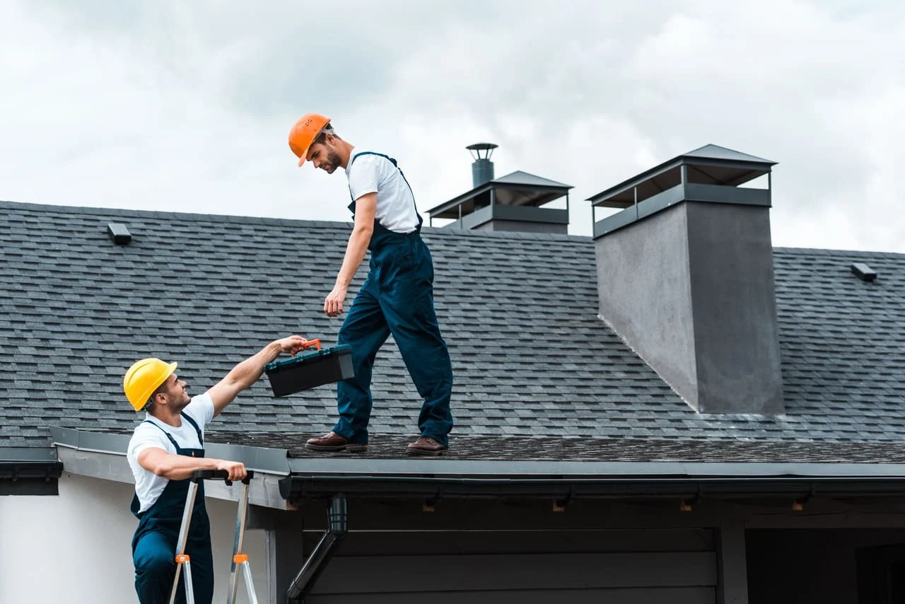 contractor hading toolbox to roofer on a roof